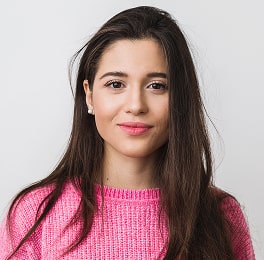 Gently smiling long dark-haired woman wearing a pink sweater
